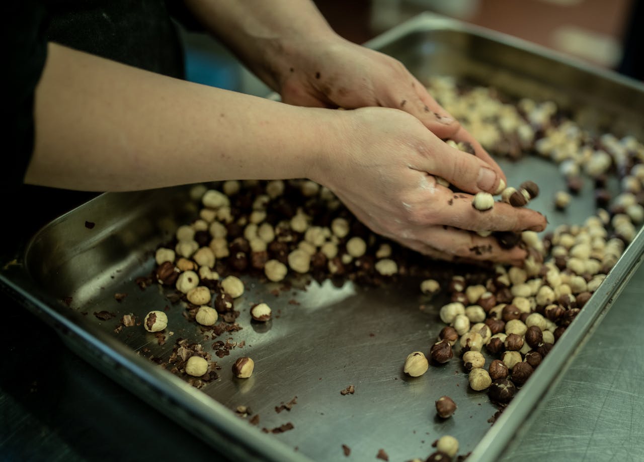 Close-up of hands sorting fresh hazelnuts on a metal tray in a kitchen setting.