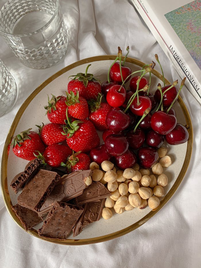 Savor fresh strawberries, cherries, hazelnuts, and chocolate on a rustic plate.